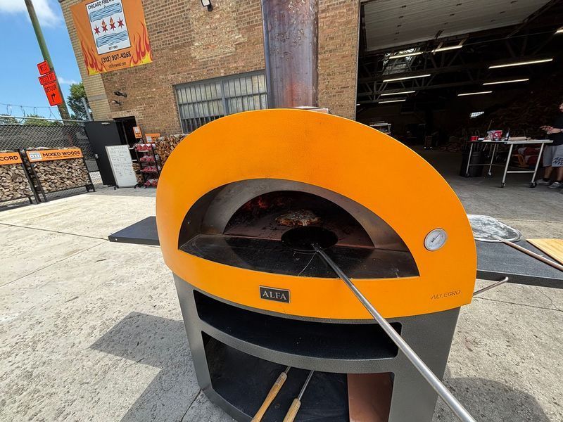 Orange outdoor pizza oven; metal peel inside.