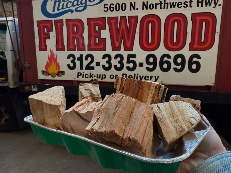 Firewood in a tray, held in front of a truck advertising Chicago Firewood, with a phone number.