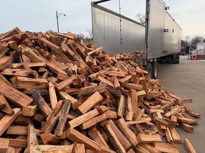 Pile of split firewood spilling out of a semi-truck trailer. Outdoors in daylight.