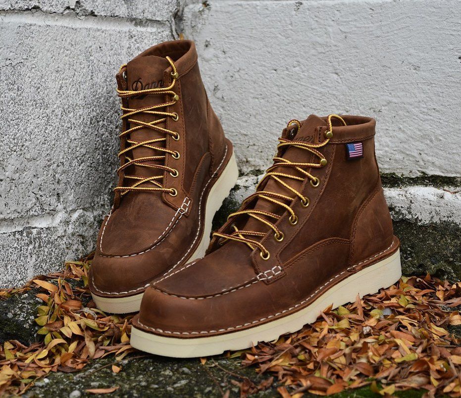 A pair of brown boots with yellow laces are sitting on a pile of leaves.