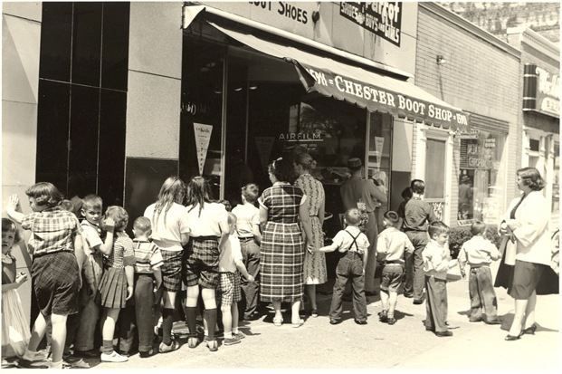 A group of people are standing outside of a store called chester boot repair