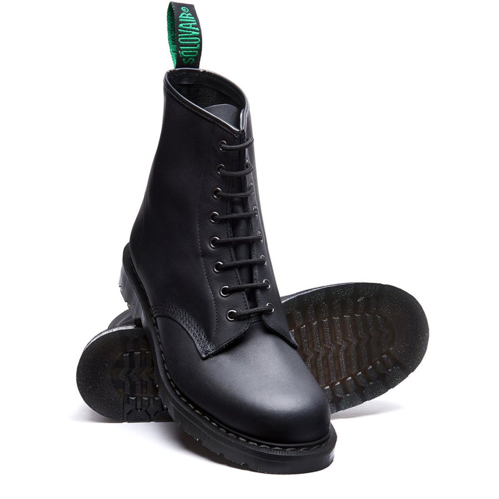 A pair of black boots with a green sole on a white background