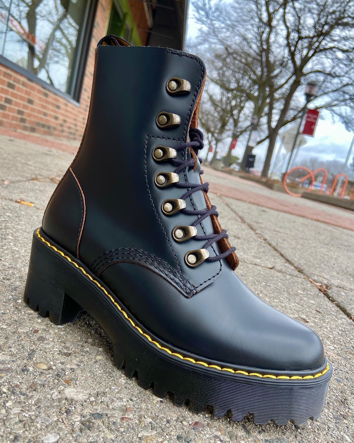 A pair of black boots with yellow laces are sitting on a sidewalk.
