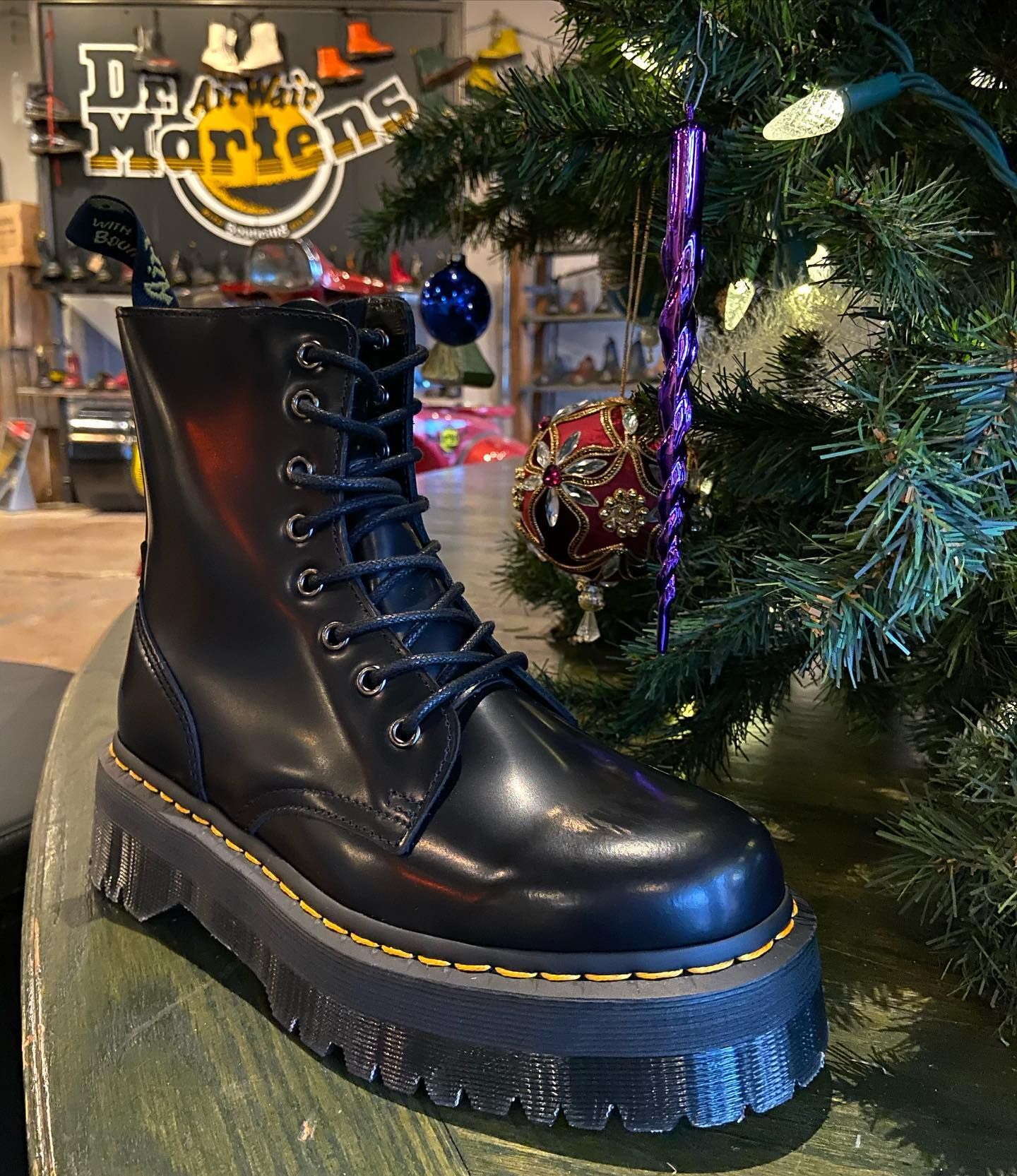A pair of black dr martens boots are sitting on a wooden table in front of a christmas tree.