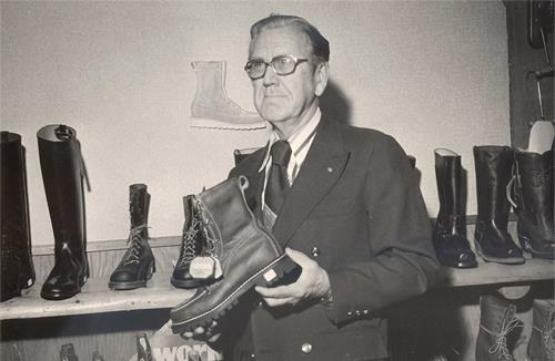 A black and white photo of a man holding a pair of boots