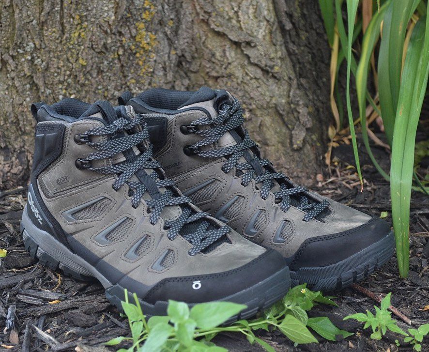 A pair of hiking boots are sitting on the ground next to a tree.