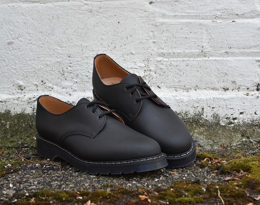 A pair of black shoes are sitting on the ground in front of a white wall.