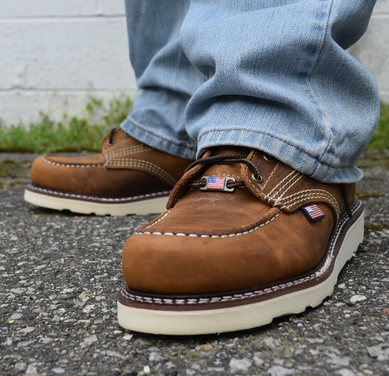 A person wearing a pair of brown shoes with an american flag on the side