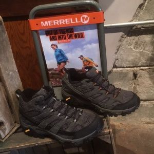 A pair of hiking boots are sitting on a shelf next to a merrell sign.
