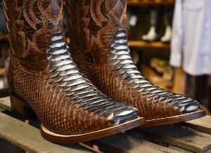 A pair of brown cowboy boots are sitting on a wooden shelf.