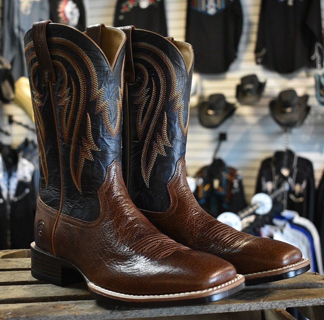 A pair of brown and black cowboy boots are sitting on a wooden table.