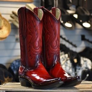 A pair of red cowboy boots are sitting on a wooden shelf.