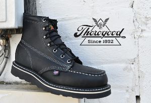 A pair of black thorogood boots are sitting on a white wall.