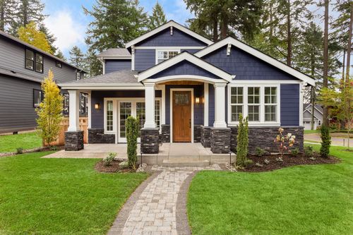 Blue two-story house with white trim, a brown door, and a stone path leading to the entrance, with lush green lawn and trees.