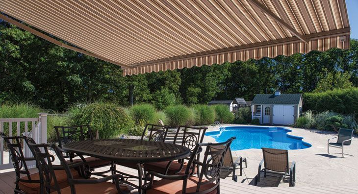 A patio with a table and chairs under an awning next to a swimming pool.
