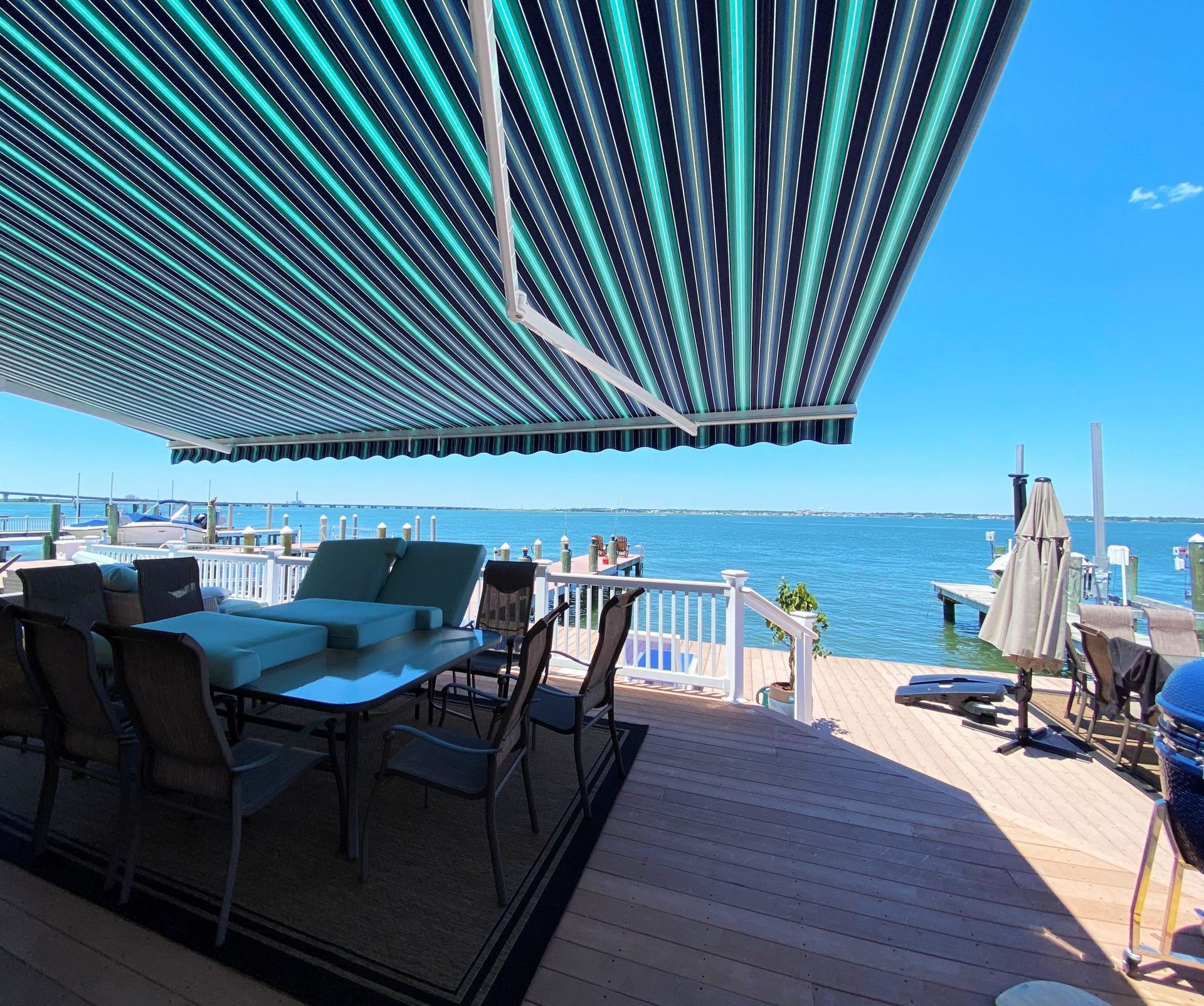 A patio with a striped awning over it overlooking a body of water