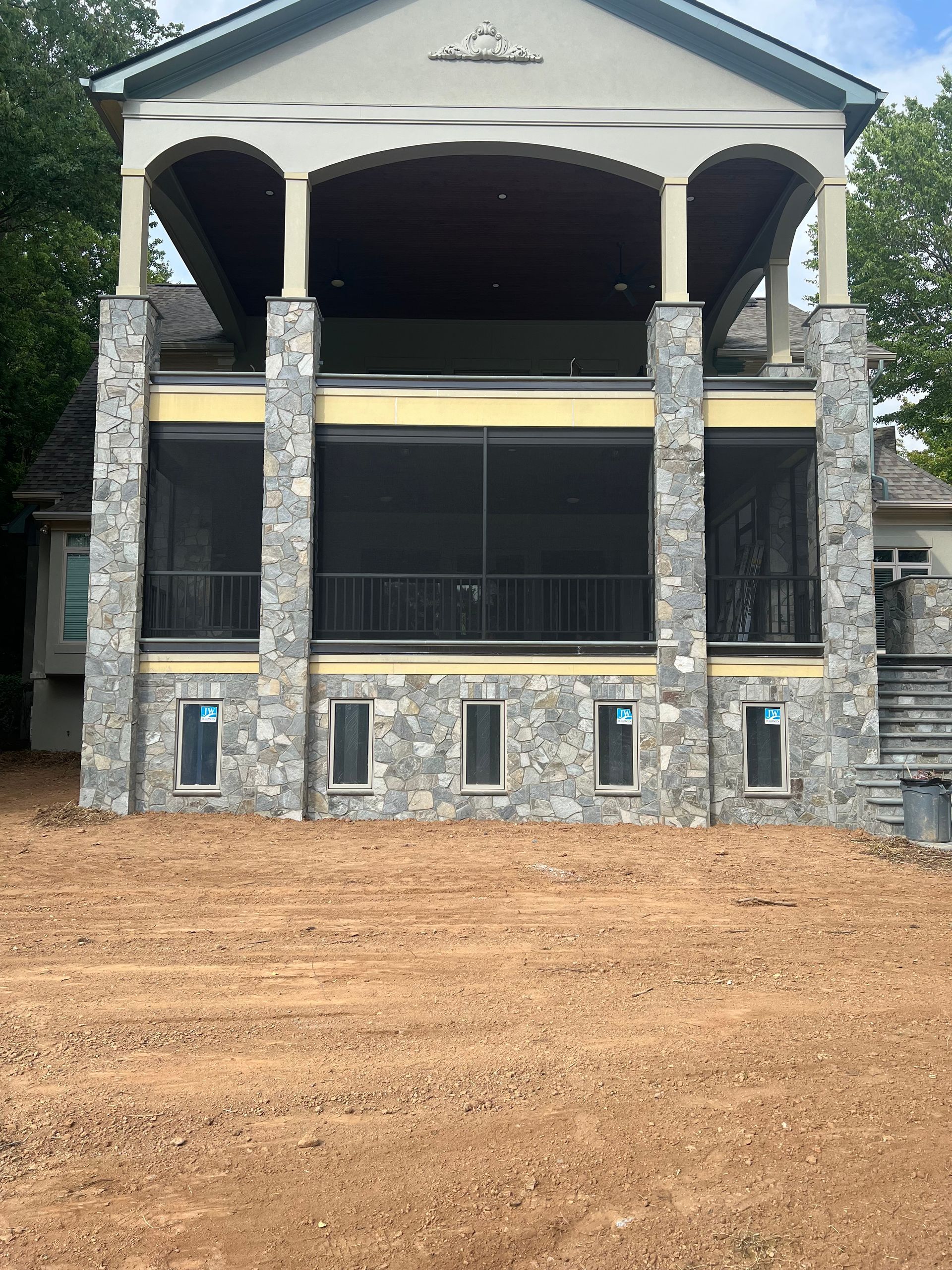 A large house with a screened in porch is sitting on top of a dirt field.