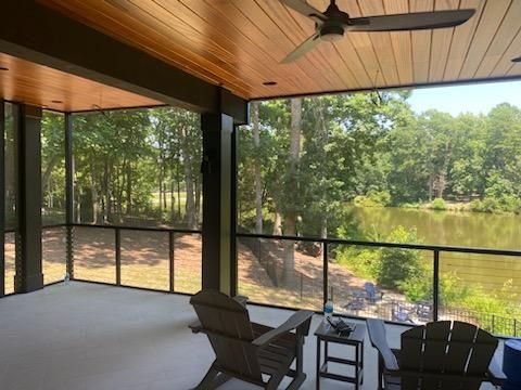 A screened-in porch with chairs and a ceiling fan overlooking a lake.