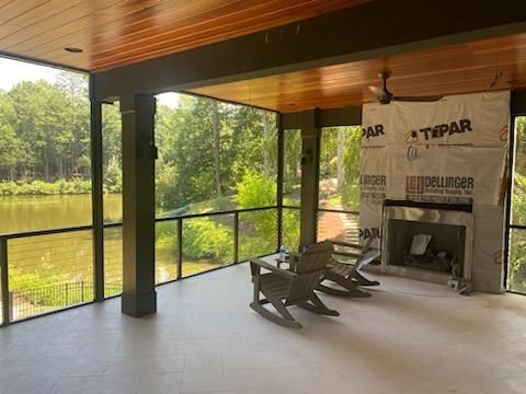 A screened-in porch with rocking chairs and a fireplace overlooking a lake.