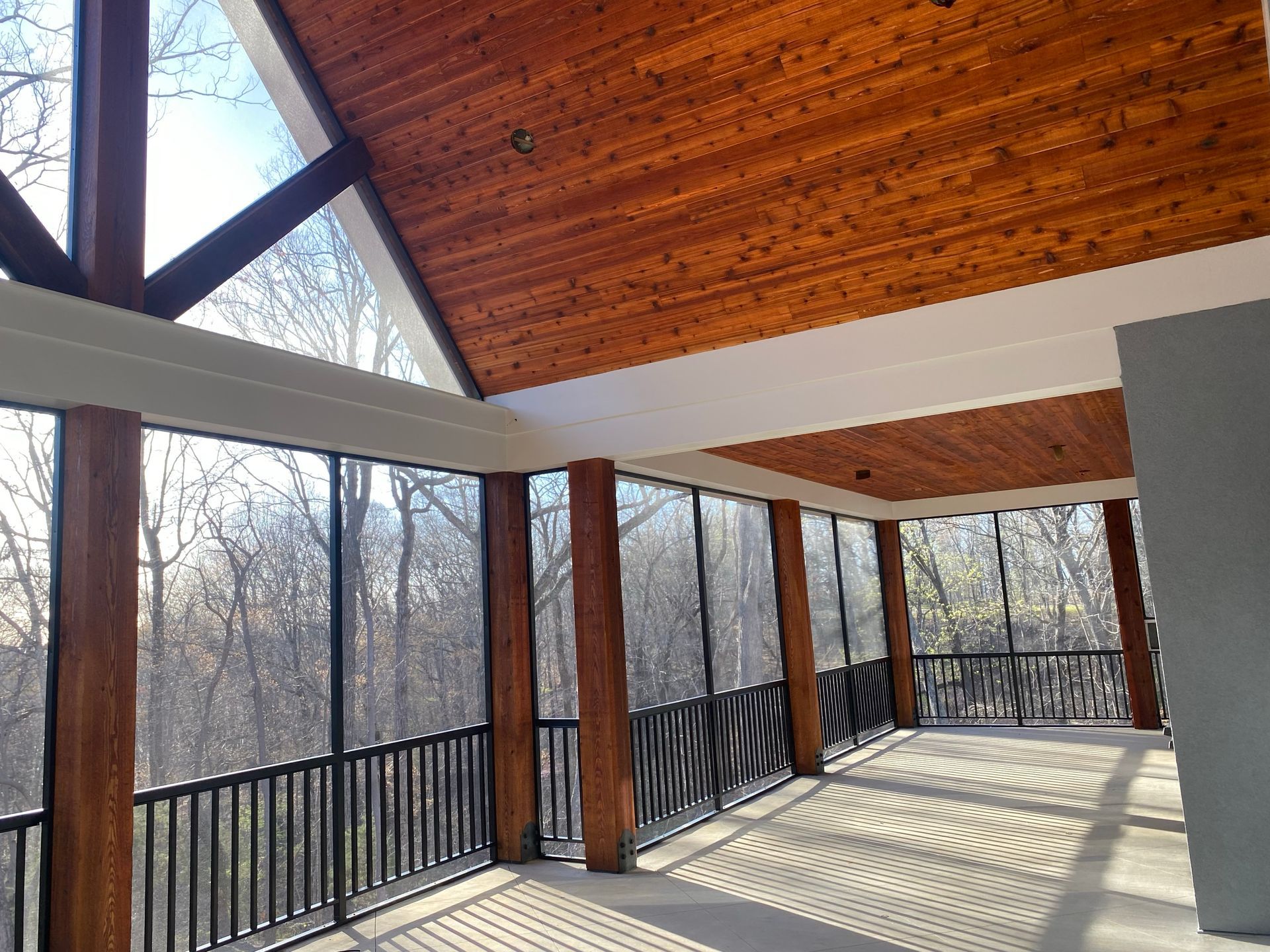 A screened in porch with a wooden ceiling and lots of windows