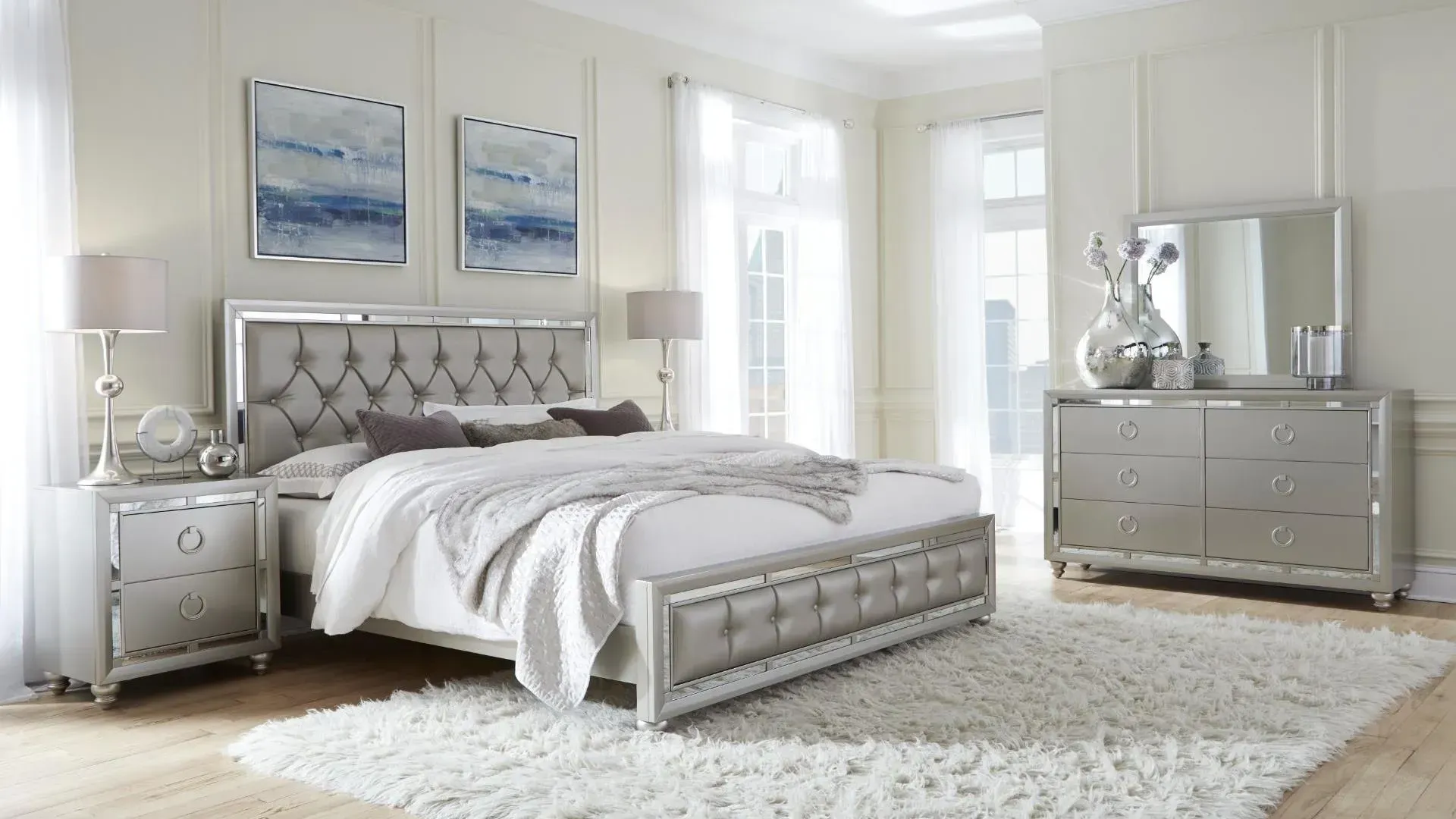 Silver bedroom set with tufted headboard, dresser, nightstand, and plush rug.