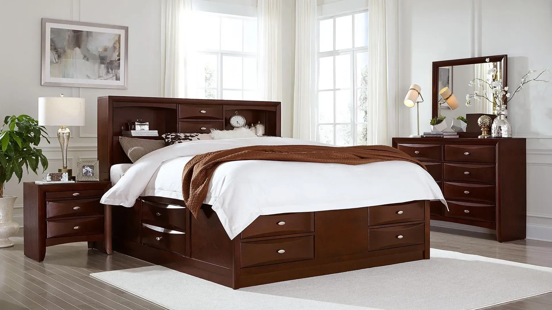 Bedroom set: dark brown storage bed, nightstand, dresser, mirror, and white rug in a bright room.