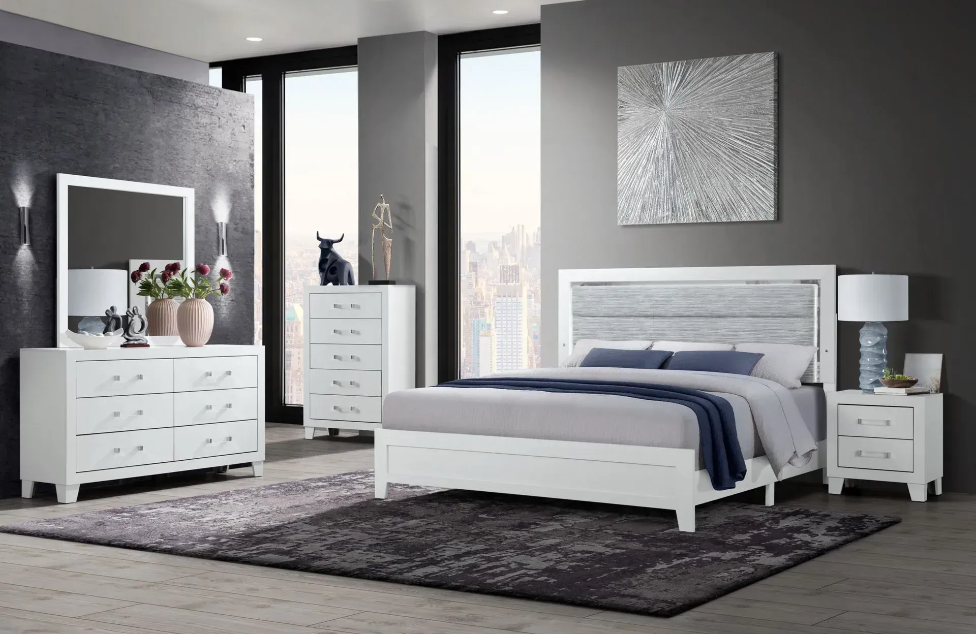 White bedroom set with bed, dresser, chest, mirror, and nightstand on a gray rug.
