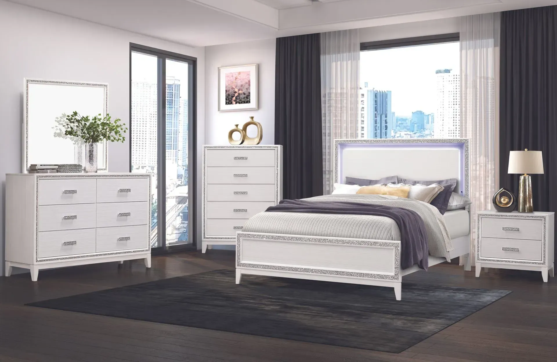 White bedroom set with bed, dresser, chest, mirror, and nightstand in front of a window.