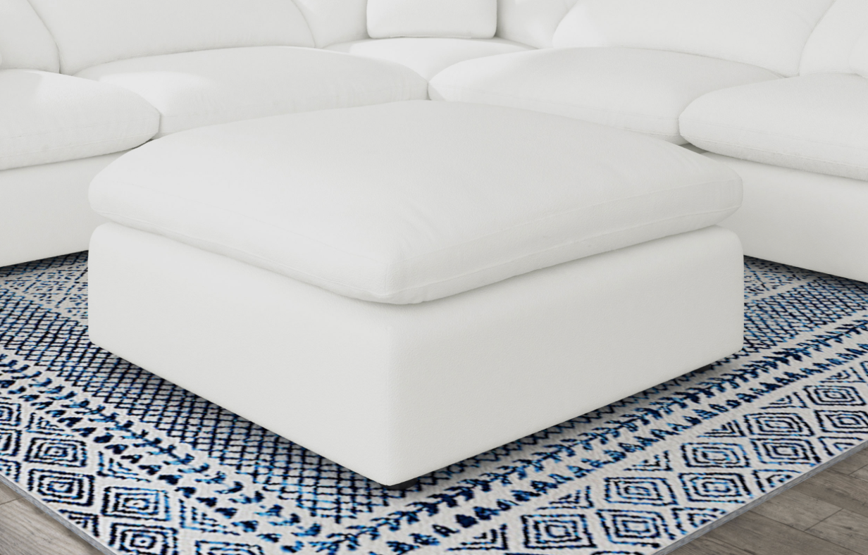 A white ottoman is sitting on top of a blue and white rug next to a white sectional couch.