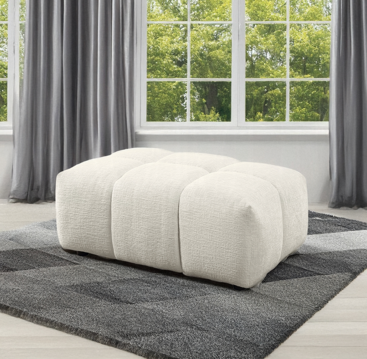 A white ottoman is sitting on a rug in front of a window.