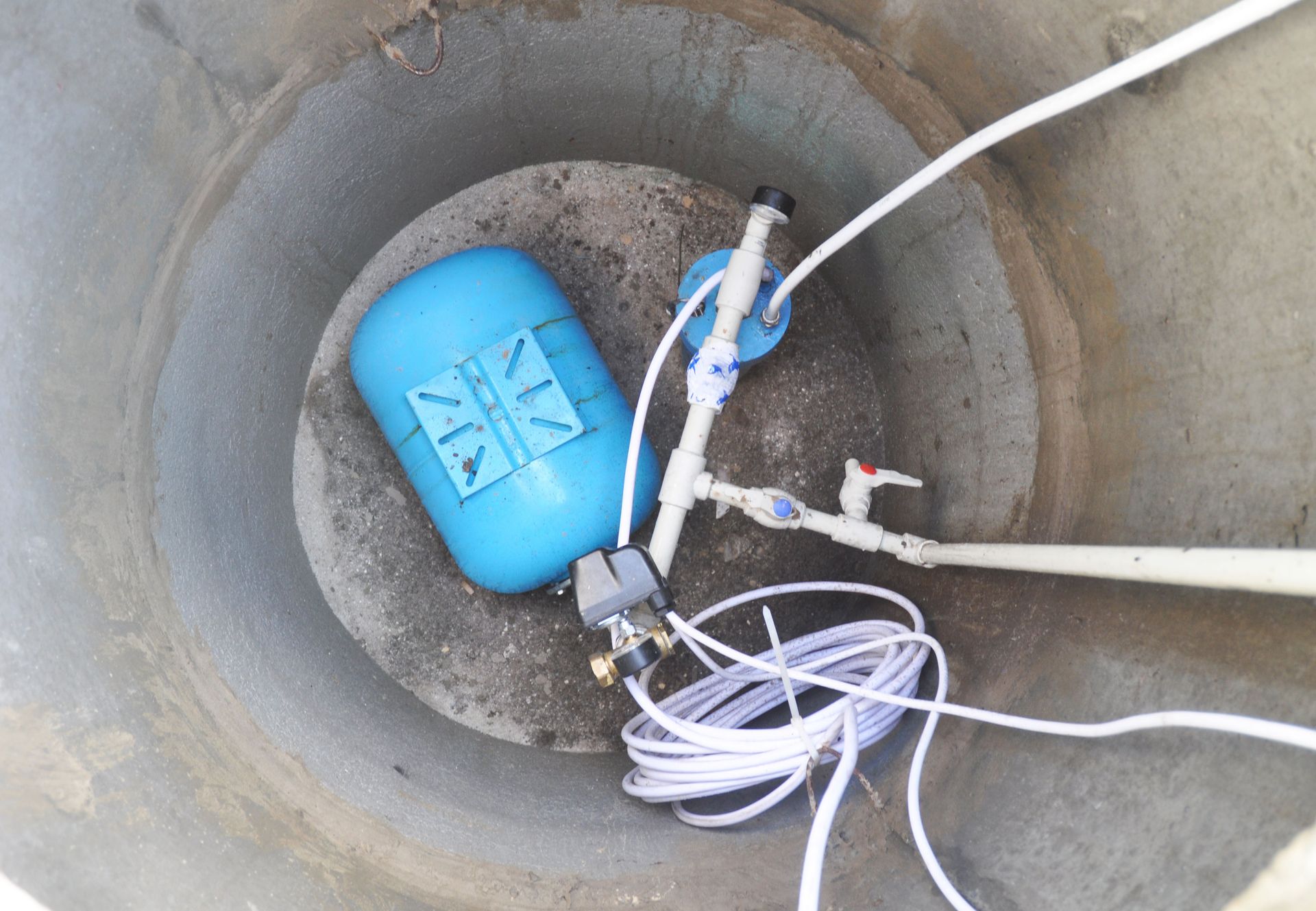 A blue water pump is sitting in the middle of a concrete hole.