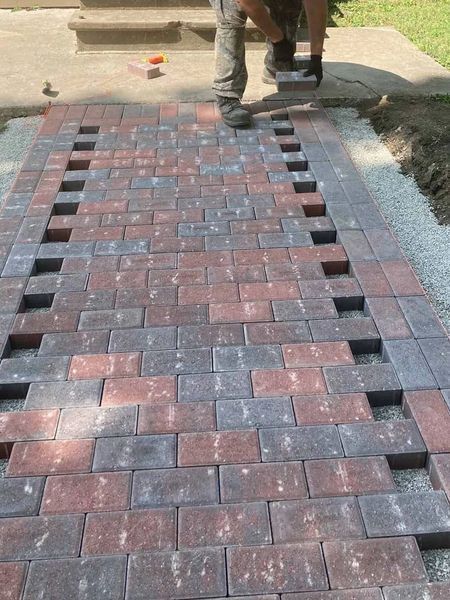 Person laying brick pavers in a walkway, alternating red and gray, with open spaces.