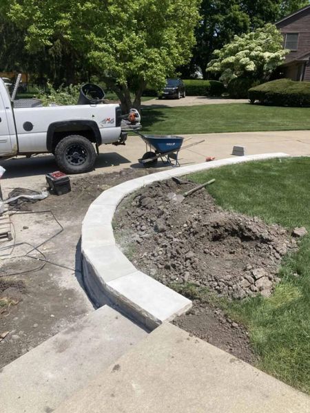 Truck parked beside a curved concrete retaining wall being built in a front yard.