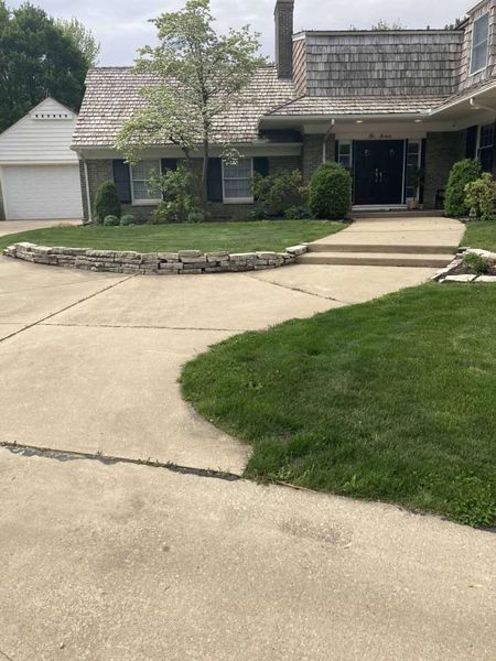 House with cedar shake roof, gray concrete driveway, front steps, and manicured lawn.