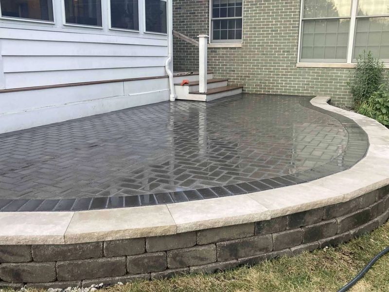 Paver patio with curved retaining wall and steps leading to house.