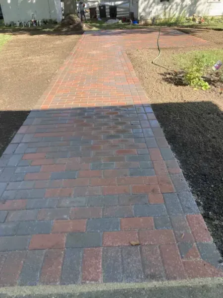 Brick walkway with red and gray bricks, leading towards a house.