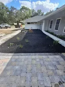 A gray-sided house with a stone path leading to a mulched front yard, under a bright blue sky.