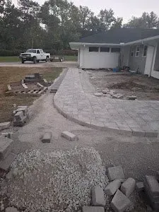 A pathway under construction made of grey bricks in front of a house; truck parked nearby.