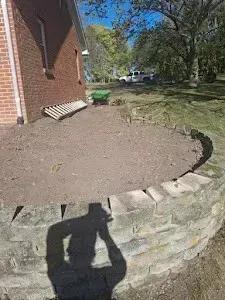 Shadow of person taking photo of a brick retaining wall and dirt area beside a brick building.