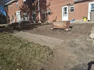 Backyard with a brick house, dirt, concrete path, and metal fire pit.