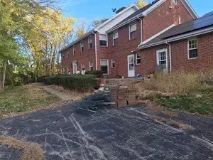 Red brick apartment building with driveway and walkway, surrounded by trees.