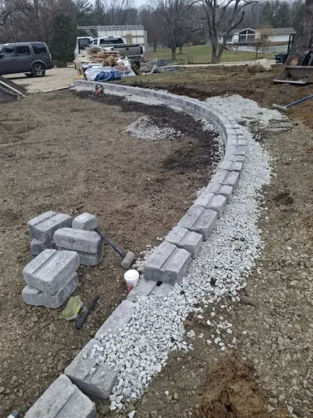 Curved pathway construction; gray pavers being laid in gravel bed on dirt.