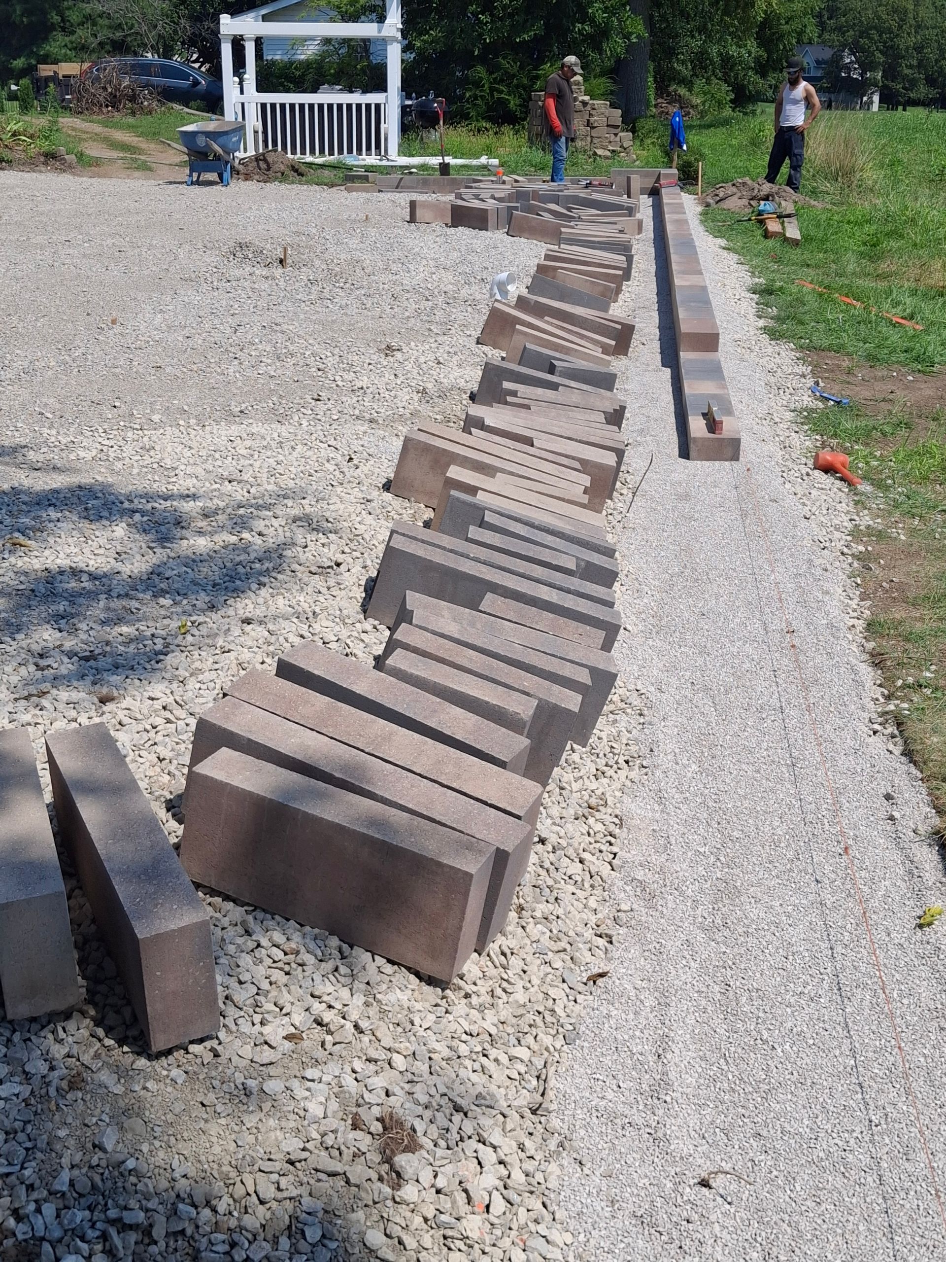 Bricks laid out on gravel, with people working on a construction project outdoors.