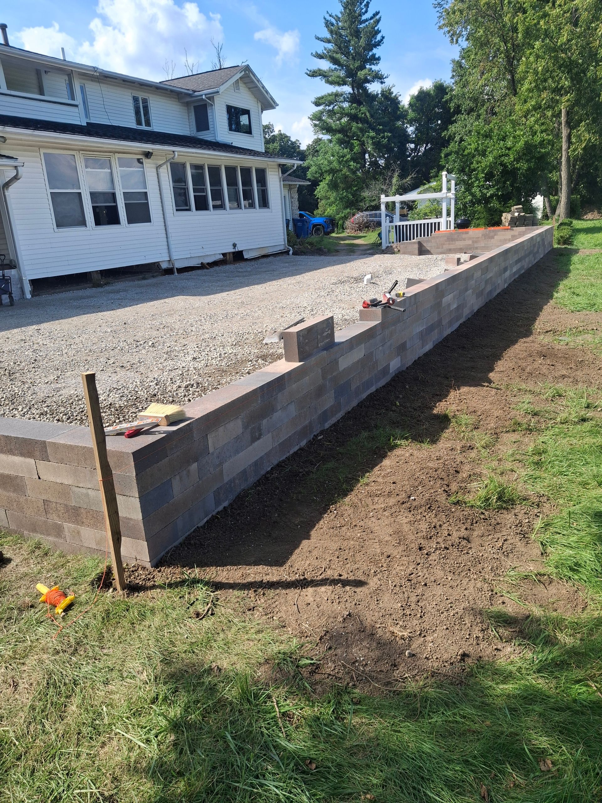 Gray retaining wall with gravel surface, next to a house on a grassy lawn.
