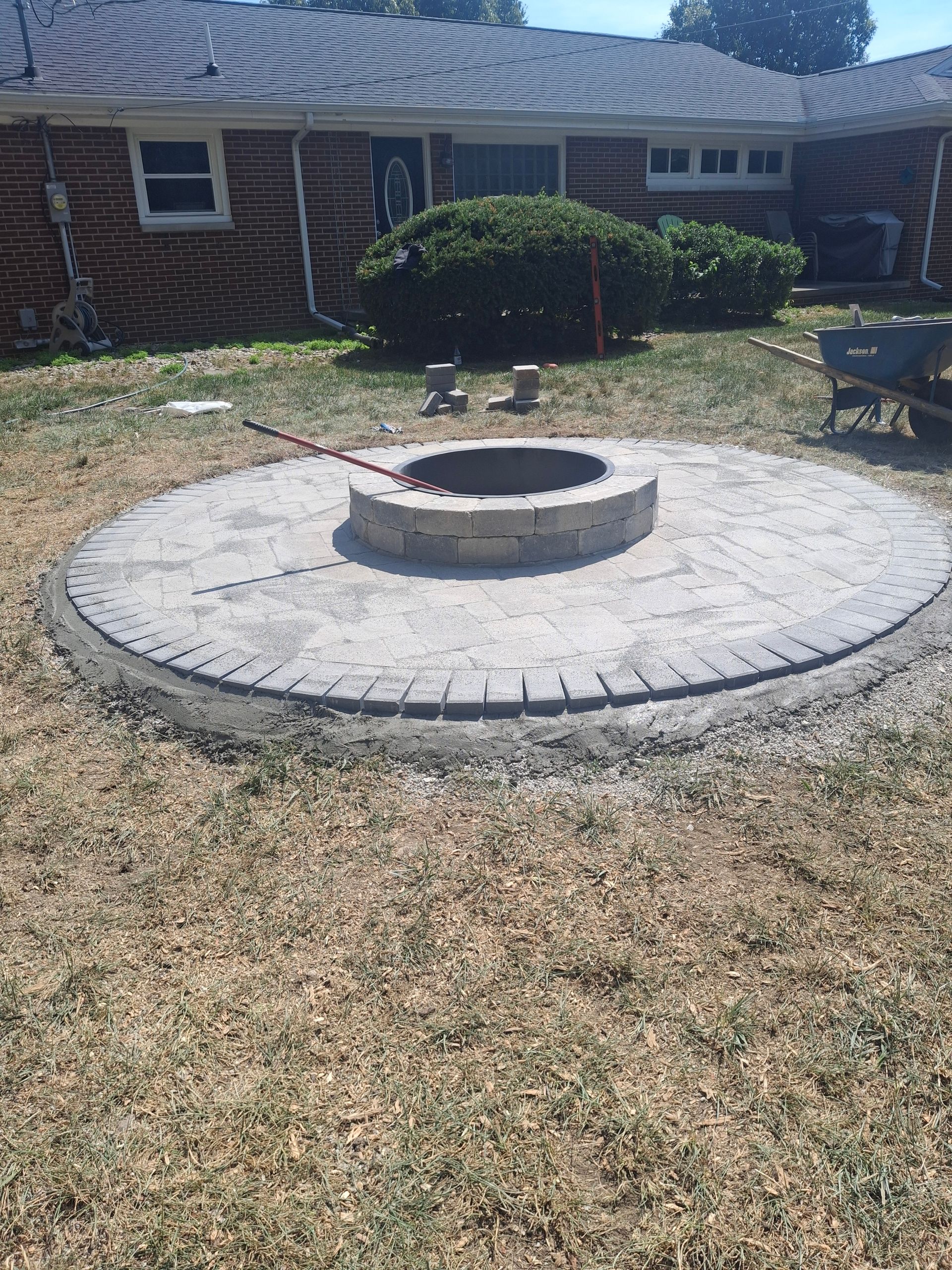 Circular brick fire pit under construction in a backyard with surrounding grass.