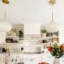 A kitchen with white cabinets, a stove, a sink, and a vase of flowers.