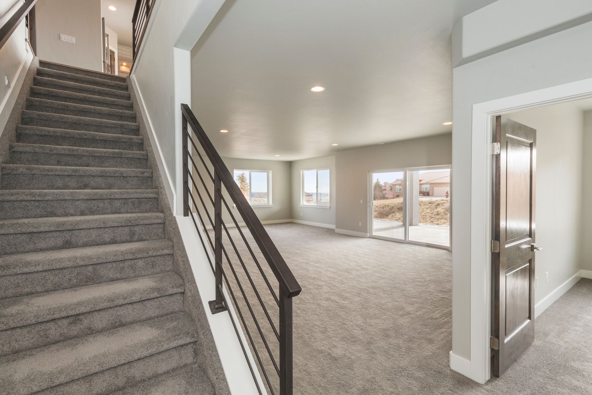 Staircase with gray carpet leads to a light-filled living space with sliding glass doors, neutral walls, and a wood door.