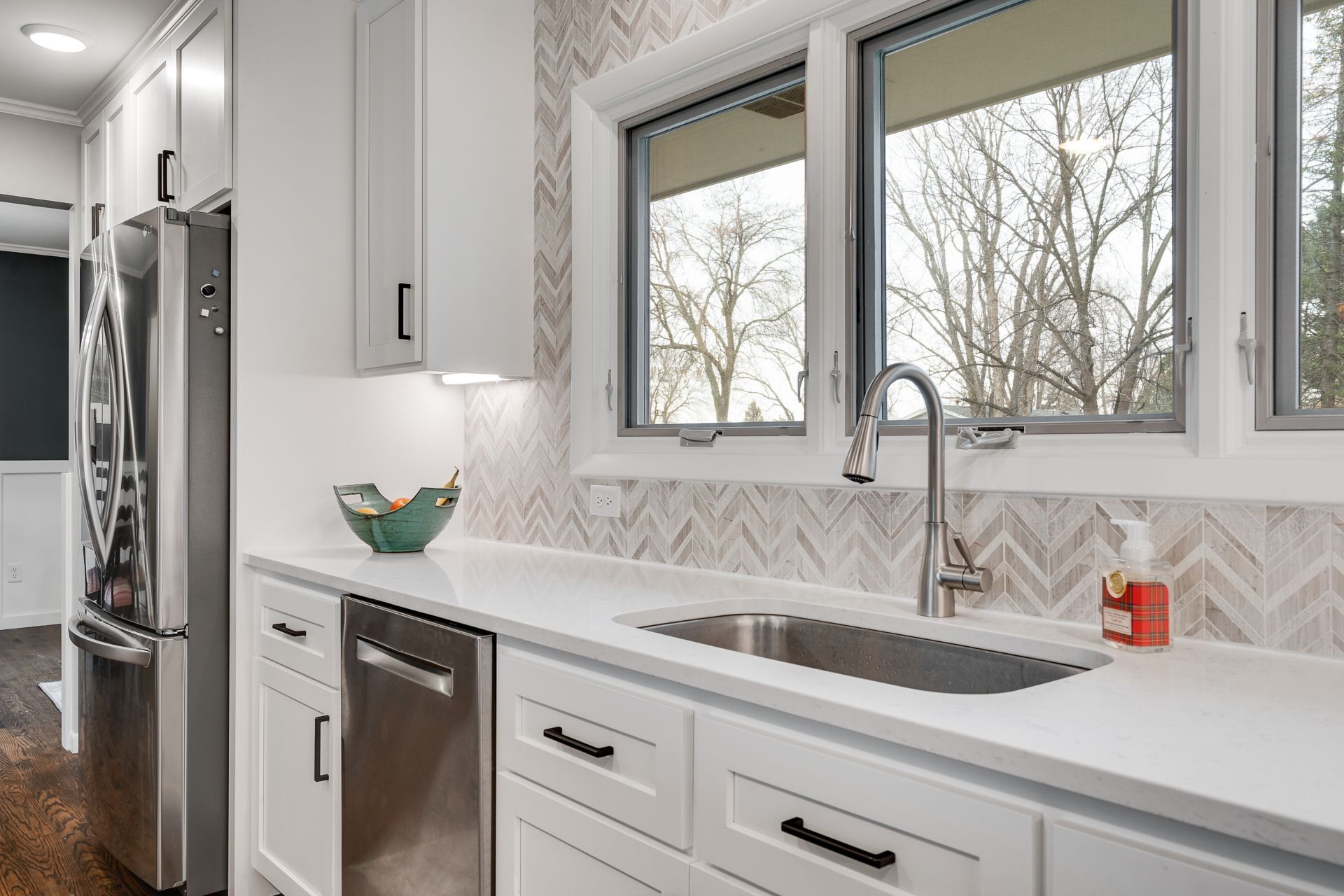 White kitchen with stainless steel appliances, white cabinets, and a sink beneath a window.