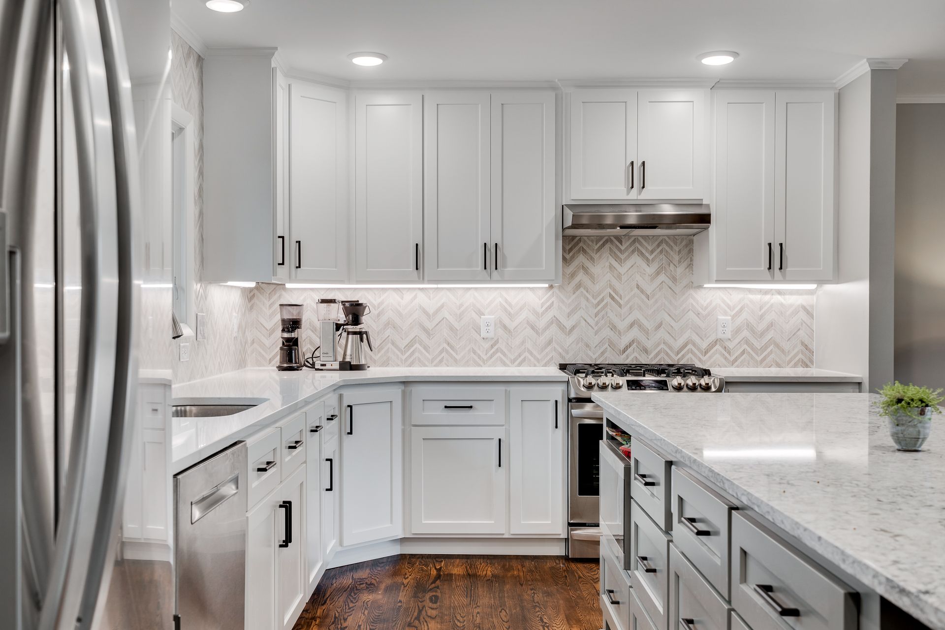 White kitchen with marble countertops, cabinets, and herringbone backsplash. Stainless steel appliances.