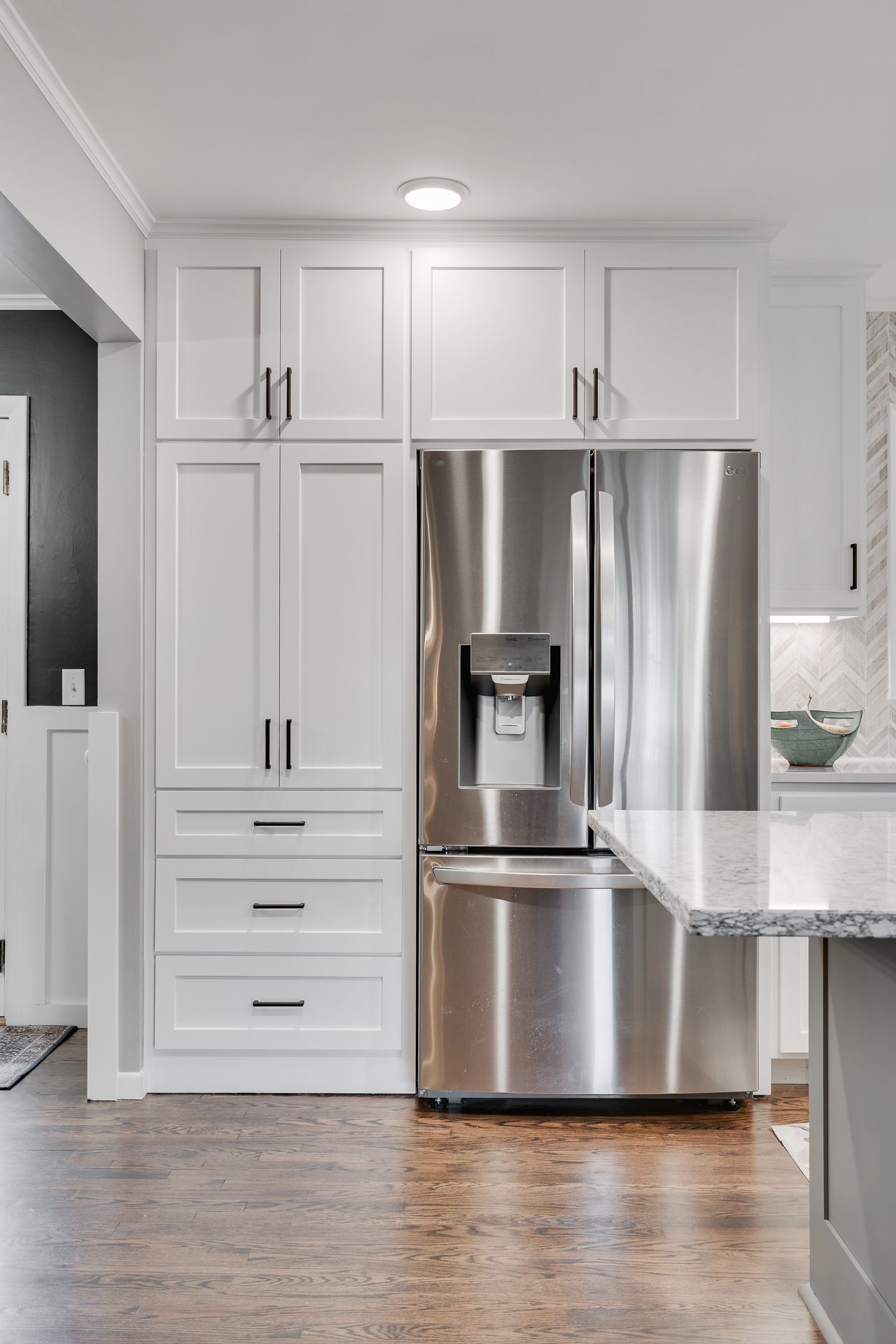 Stainless steel refrigerator beside white pantry cabinets in a kitchen.
